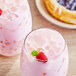 Two glasses of pink drinks with ice and berries on top.