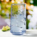 A close-up of an Anchor Hocking Coastal Blue cooler glass filled with water, ice, and a lime slice.