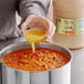 A person pouring Marie Sharp's grapefruit habanero hot sauce into a pot of food.