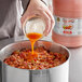 A person pouring orange liquid hot sauce into a pot of food.