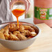 A person pouring Marie Sharp's hot sauce into a bowl of chicken wings.