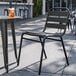 A Lancaster Table & Seating black powder-coated steel outdoor side chair on a patio next to a table with a drink.