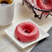 A red Southern Roots vegan red velvet cake donut on a white plate next to a cup of coffee.
