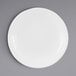 A white Elite Global Solutions round melamine plate with a rim on a gray surface.
