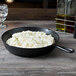 An Elite Global Solutions Illogical Faux Cast Iron fry pan with mashed potatoes and chives on it.