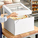 A woman opening a Southern Champion cake box with a window to reveal a cake inside.