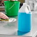 A person using a translucent jug of blue liquid to clean a counter.