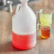 A white translucent plastic jug filled with red liquid next to a measuring cup.