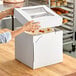 A hand opening a Southern Champion white bakery box with a clear window.