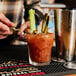 A person holding a skewer with a bloody mary and a celery stick.