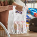 A man holding an Inteplast plastic T-shirt bag in front of a cash register.