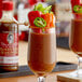 A glass of liquid with Demitri's Chilies and Peppers Bloody Mary Concentrated Seasoning mix and a garnish stick on a table.