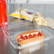 A Dart clear plastic container with a hot dog, chips, and a drink on a counter.