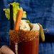 A hand holding a glass of a bloody drink with a Demitri's Bacon Rim Shot rimmed pickle garnish.