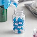 A hand in blue gloves pouring pills into a clear PET packer bottle.