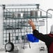 A man hanging a rack of pots and pans on a Metro Custom SmartWall shelving unit in a professional kitchen.