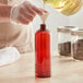 A person pouring liquid into a Boston Round PET amber bottle.