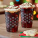 Two Choice snowflake PET plastic cold cups filled with a brown iced drink with whipped cream and cookies on a table.