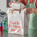 A person putting a styrofoam box into a white Source Direct Inc. T-shirt bag.