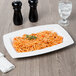 A Libbey white rectangular porcelain bowl filled with spaghetti on a table with a glass of water.