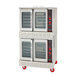 A double-deck electric convection oven with glass doors and red control knobs, mounted on red caster wheels.