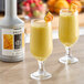 Two glasses of yellow liquid with mango slices on top.