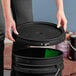 A person using a BWAY black round pail cover to open a black bucket.