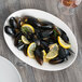 A Libbey white porcelain oval platter with mussels and lemon slices on a brown table.