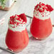 Two glasses of red Cappuccine Supreme Red Velvet frappes with whipped cream and red crumbs.