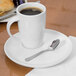 A Libbey white porcelain saucer with a cup of coffee and a spoon on it.