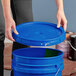 A woman holding a BWAY blue plastic bucket with a lid.