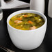 A bowl of bouillon with vegetables and meatballs on a white table.