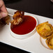 A person dipping bacon on a stick into sauce on a Libbey rectangular porcelain tray with 3 wells.