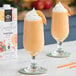 Two glasses of peach smoothie with straws and a peach on a table in a smoothie shop.