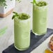 Two glasses of Cappuccine Supreme Matcha Latte Frappe with mint leaves on top on a black tray.