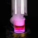 A close up of a Flavour Blaster round color-changing LED light coaster with a glass of pink and purple liquid and smoke.