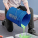 A woman pouring green paint into a blue BWAY bucket with a metal handle.