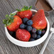 A Libbey Royal Rideau white stacking porcelain fruit bowl filled with strawberries and blueberries with a fork.