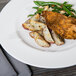 A Libbey round white porcelain plate with food including potatoes and chicken on a wood table.