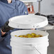 A woman in a chef's uniform holding a BWAY white pail with a white plastic lid.