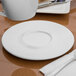 A Libbey Royal Rideau white porcelain saucer on a white plate with a spoon and fork.