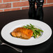 A Libbey white porcelain plate with salmon and green beans on a table with a fork.