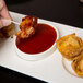 A person dipping a bacon on a toothpick into sauce using a Libbey Royal Rideau white porcelain bowl.