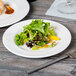 A plate of salad and a fork on a Libbey white porcelain plate on a wood table.