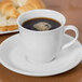 A Libbey Royal Rideau white porcelain cup of coffee on a saucer with a bagel.