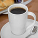 A Libbey Slenda white porcelain mug filled with coffee on a plate with a spoon.