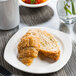 A Libbey Slenda white square porcelain plate with a croissant on a table.