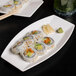 A Libbey rectangular white porcelain serving tray with sushi on a black surface.