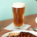 A Libbey Gibraltar cooler glass filled with beer on a table with food.