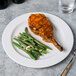 A Libbey white porcelain plate with a pork chop and green beans on it.